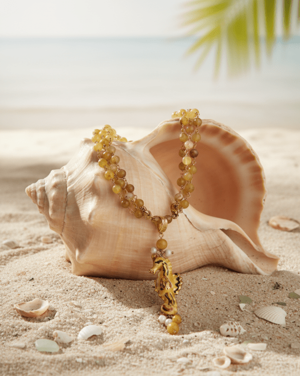 Collar caballito marino amarillo con cuentas doradas sobre concha en la arena