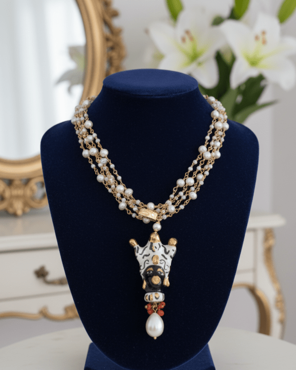 Collar Otello de Haydée en un busto azul junto a lirios blancos, con perlas y testa di moro de cerámica siciliana