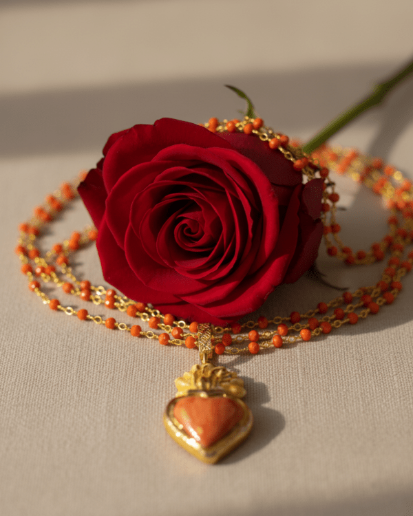 Collar Haydée con colgante de corazón rojo sobre rosa roja en fondo neutro