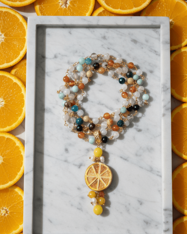 Collar Orangina de Haydée sobre una bandeja de mármol rodeada de naranjas, con colgante de cerámica siciliana