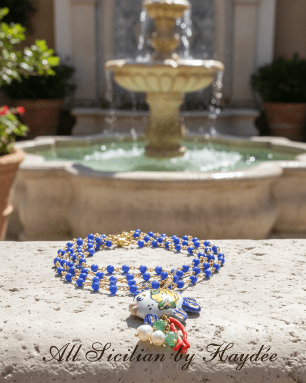 Collar Pez al Limone de Haydée sobre una fuente de piedra, con cuentas azules y pez de cerámica siciliana