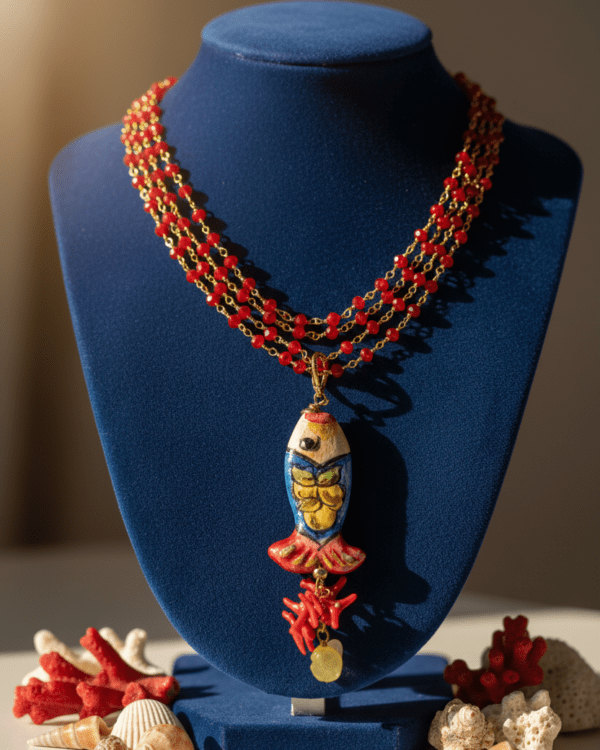 Collar Sam de Haydée en un busto azul, con varias vueltas de cuentas rojas y colgante de cerámica siciliana