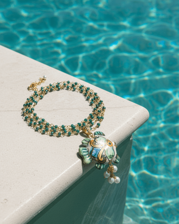 Collar Tiny de Haydée en el borde de una piscina, con cuentas verdes y colgante de cerámica siciliana